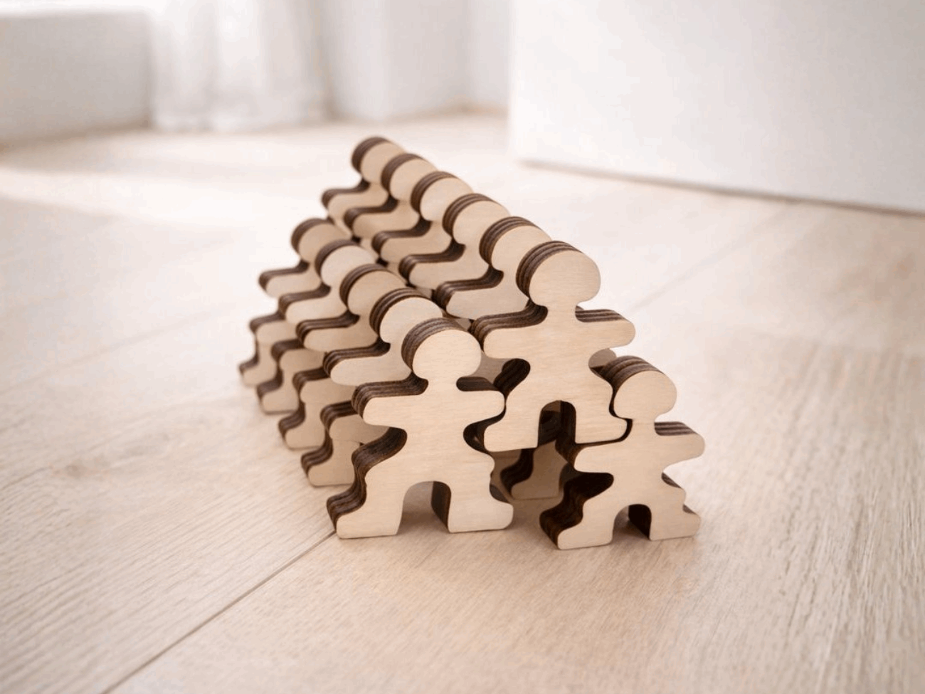 Stacked Master Buddies wooden figures arranged in a pyramid shape on a light wooden floor